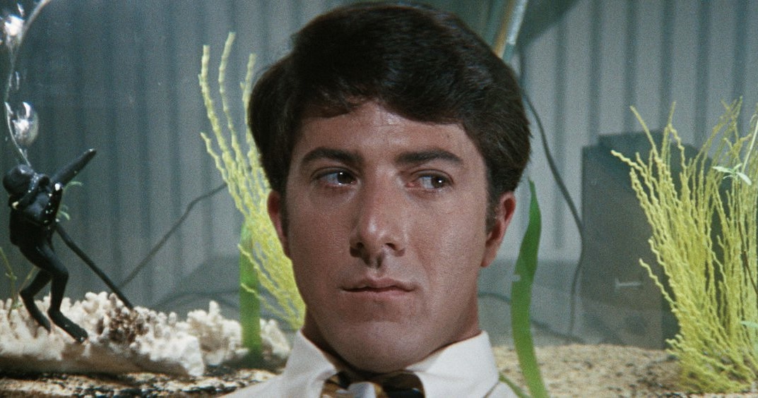 Benjamin Braddock, portrayed by Dustin Hoffman, sits in lonely contemplation framed by the water of a fish tank. 